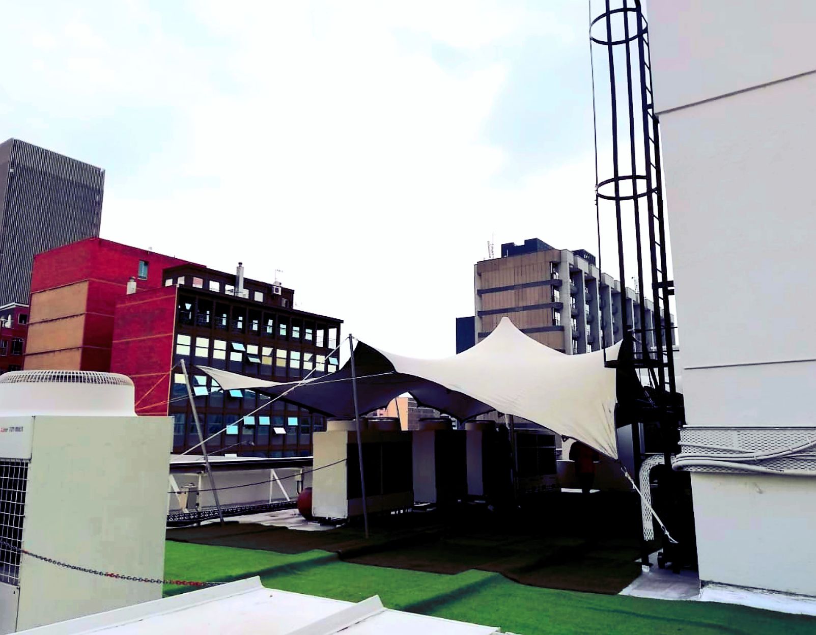 Grey Tent Erected On A Rooftop In Between Buildings With Green Turf.
