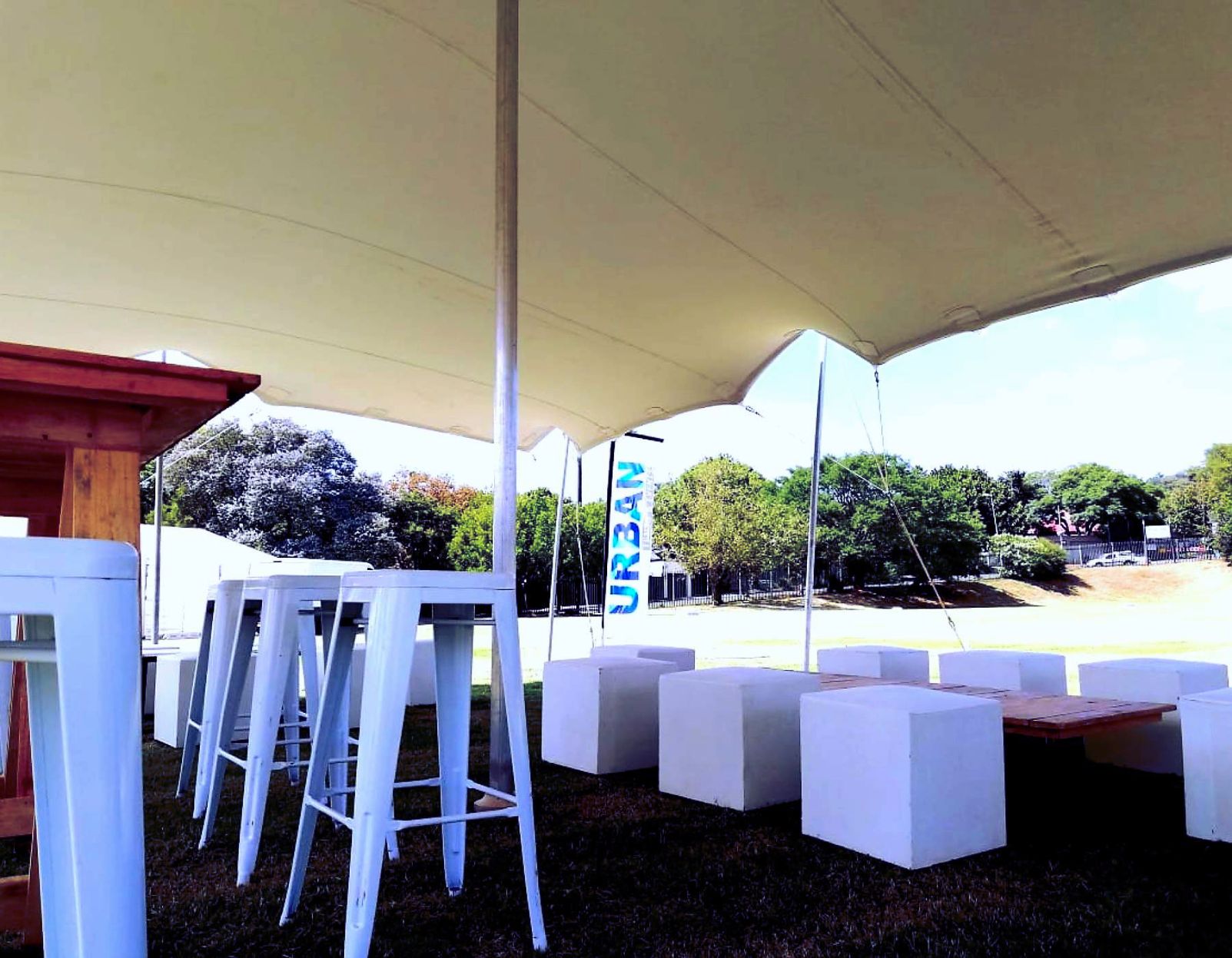 White Steel Bar Stools With White Ottomans And Wooden Table Under A Tent.