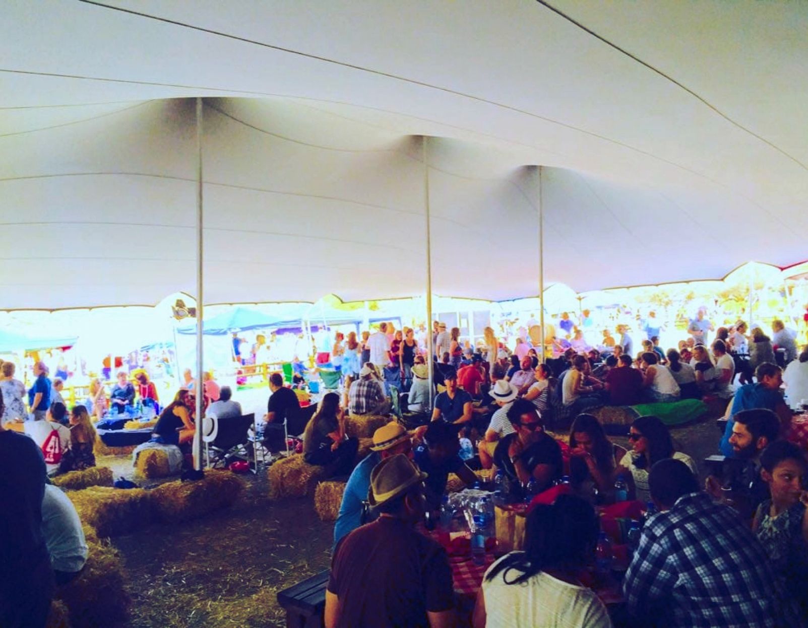 Crowd At A Wine Festival Seated Under A Large White Stretch Tent.